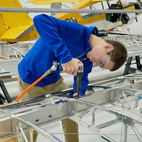 A high school boy using a power drill while building the frame of an airplane wing